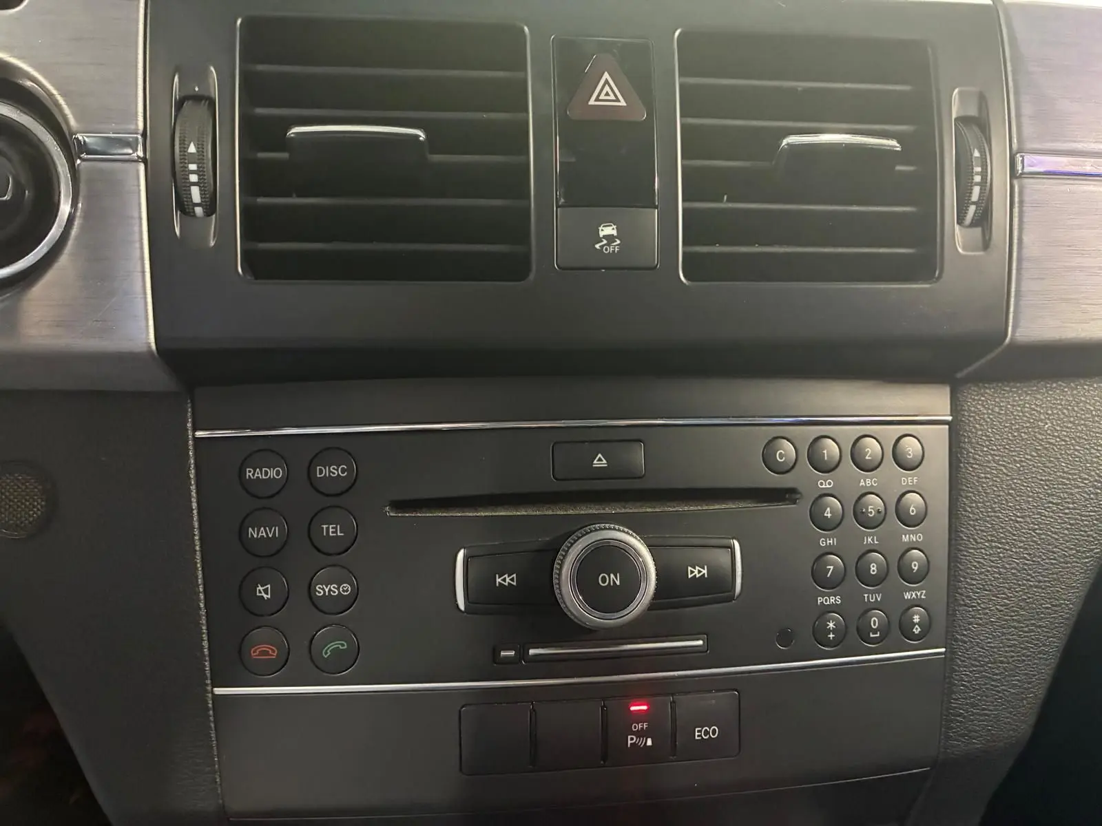 Vue rapprochée de la console centrale noire du Mercedes GLK 2012 avec commandes radio, climatisation et boutons de sécurité.