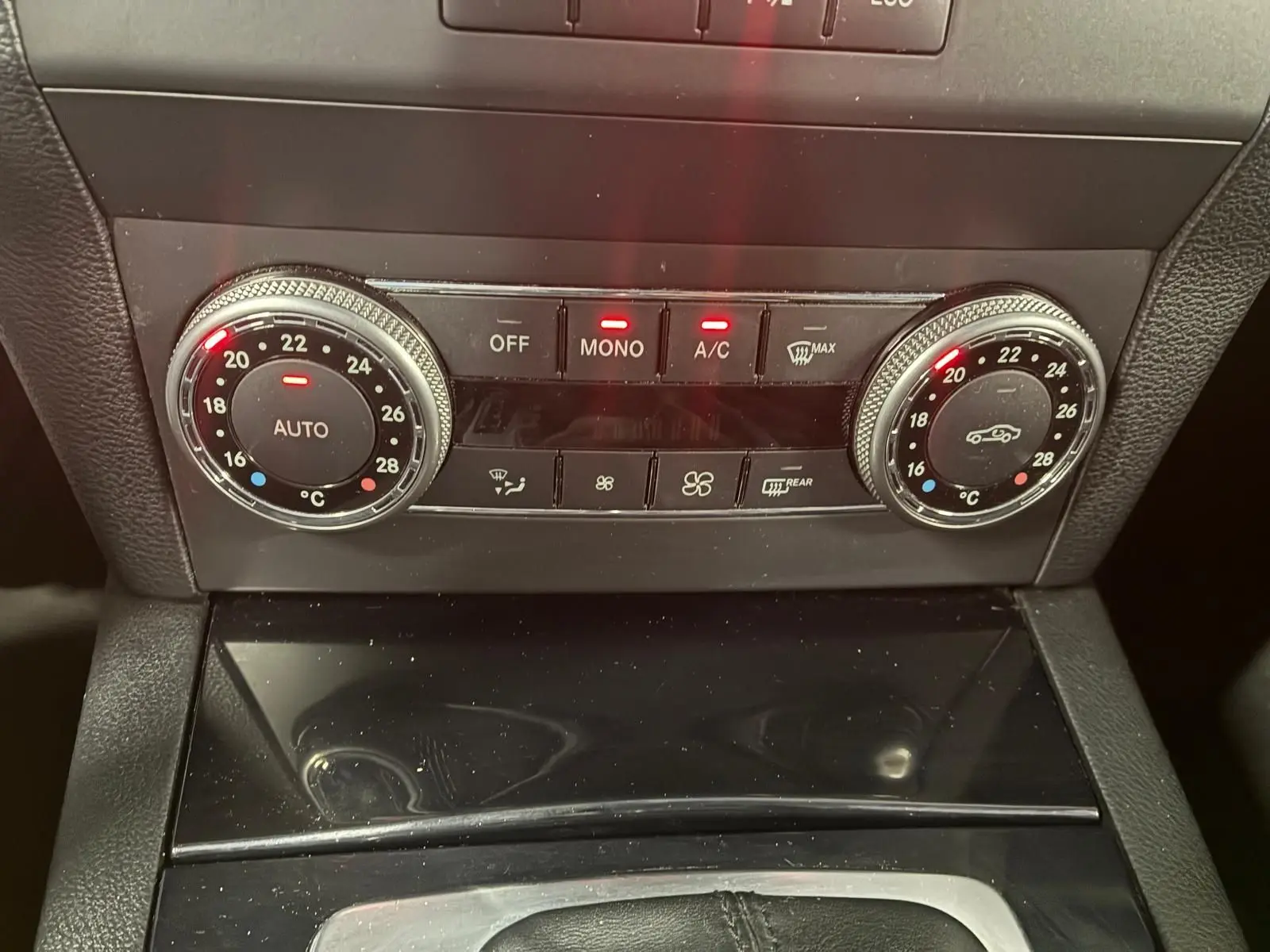 Gros plan sur la console centrale noire du Mercedes GLK 2012, montrant les commandes de climatisation automatique avec affichage digital.