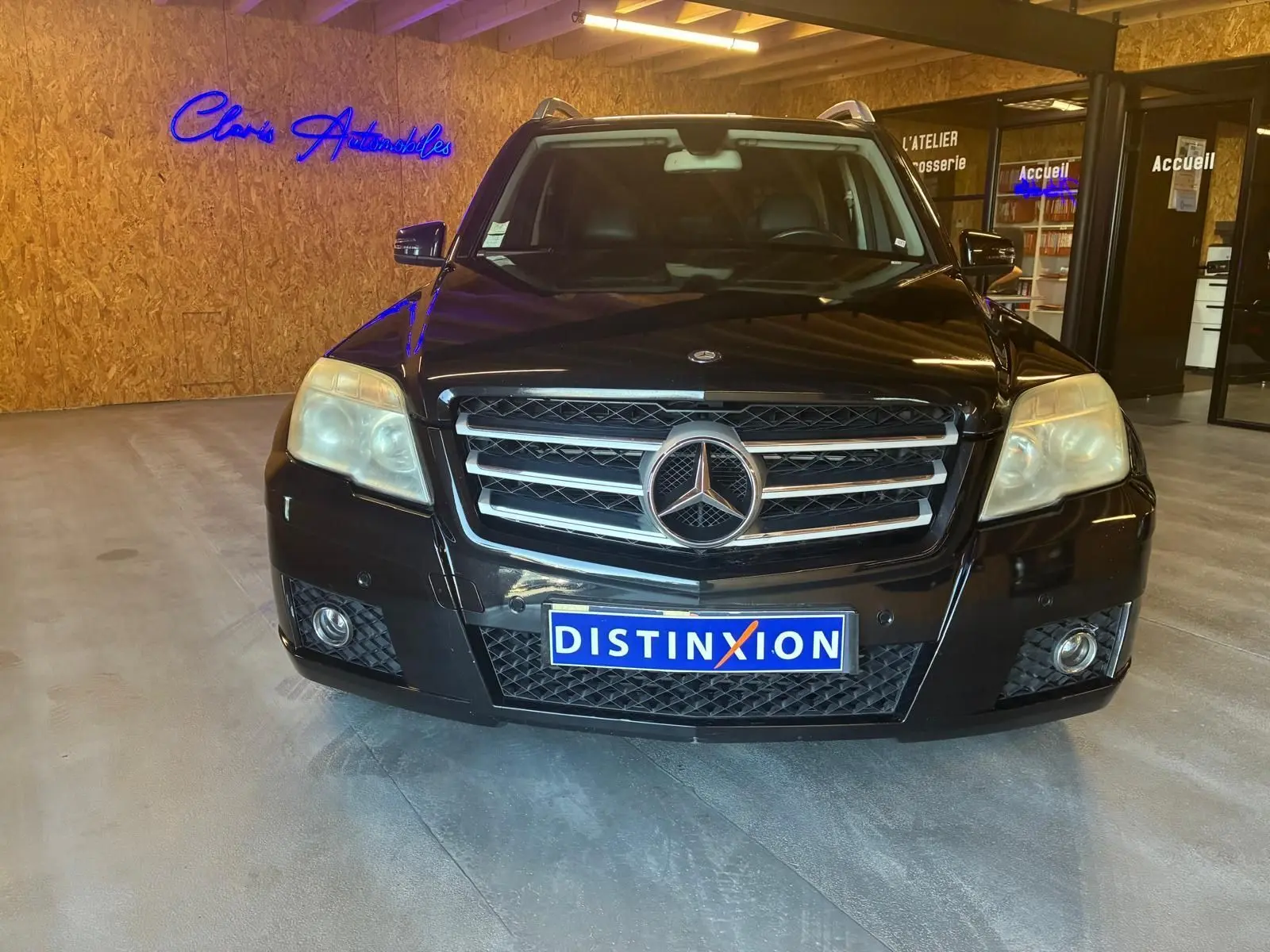 Vue de face d'un Mercedes GLK noir 2012 avec calandre chromée et plaque d'immatriculation DISTINXION en intérieur showroom.