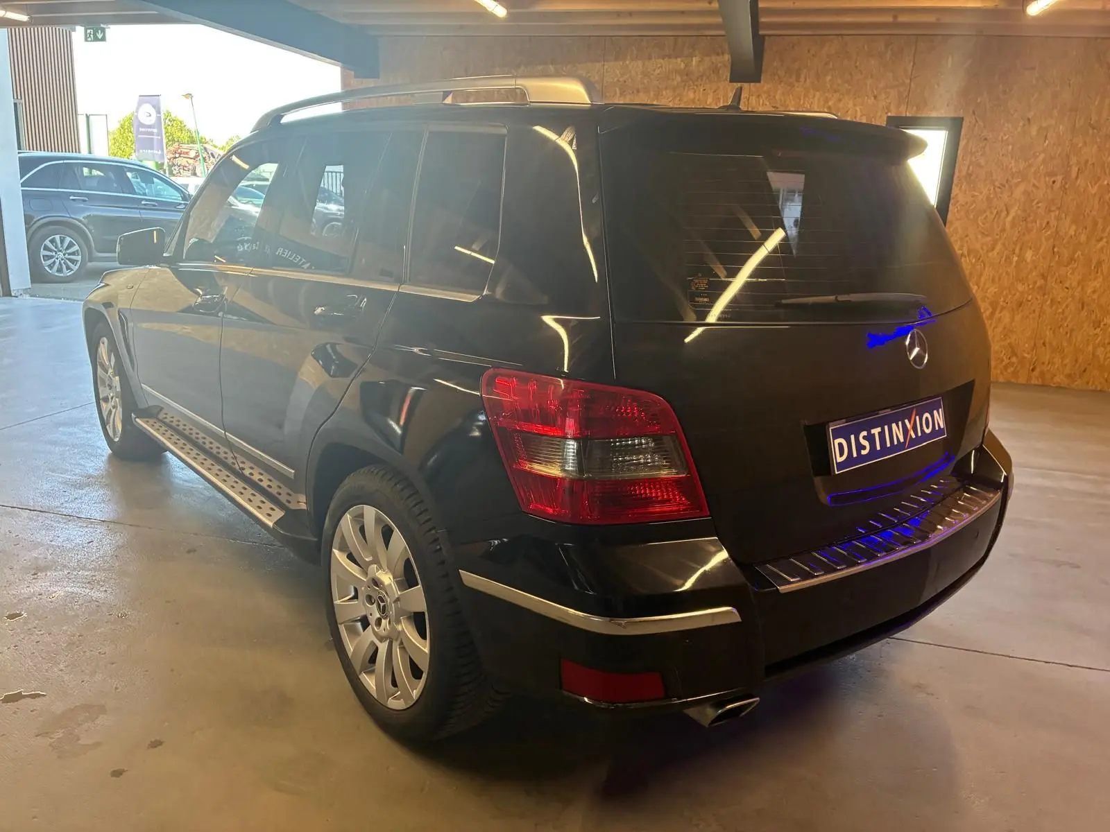 Mercedes GLK noir vu en 3/4 arrière droit, avec feux arrière rouges et jantes argentées dans un garage.