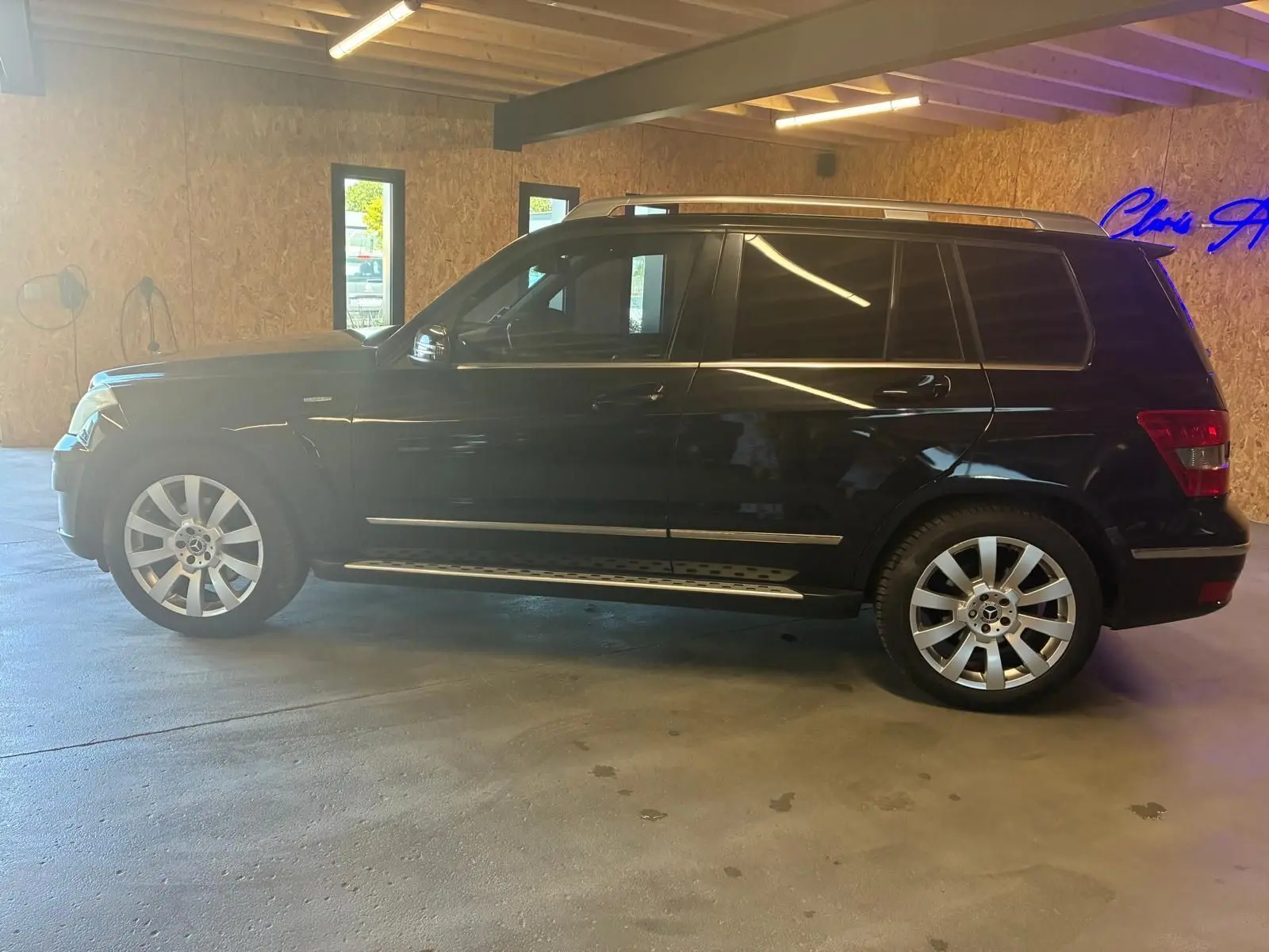 Vue de profil côté gauche d'un Mercedes GLK noir 2012 avec jantes alliage et barres de toit argentées.