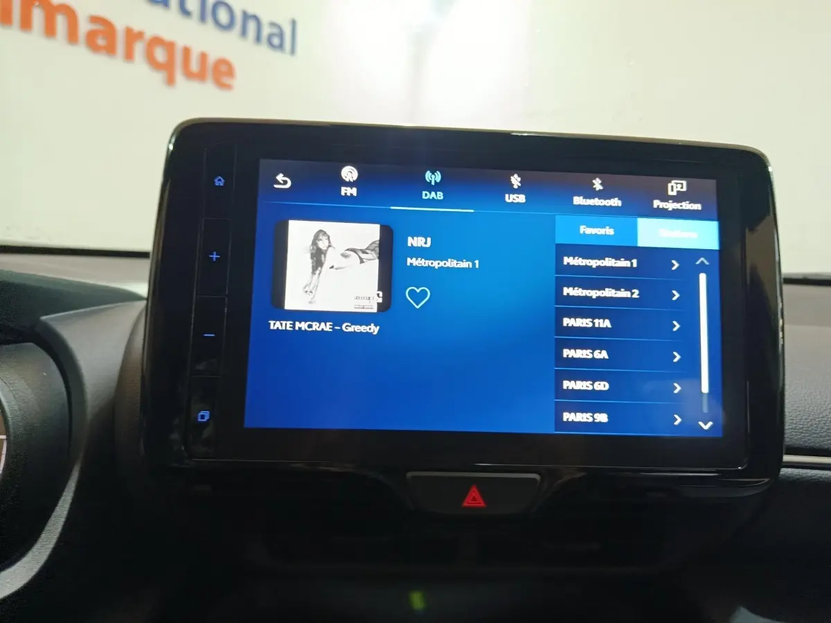 Écran tactile central affichant la radio DAB dans l'habitacle d'une Toyota Yaris Cross gris foncé, vue de face.