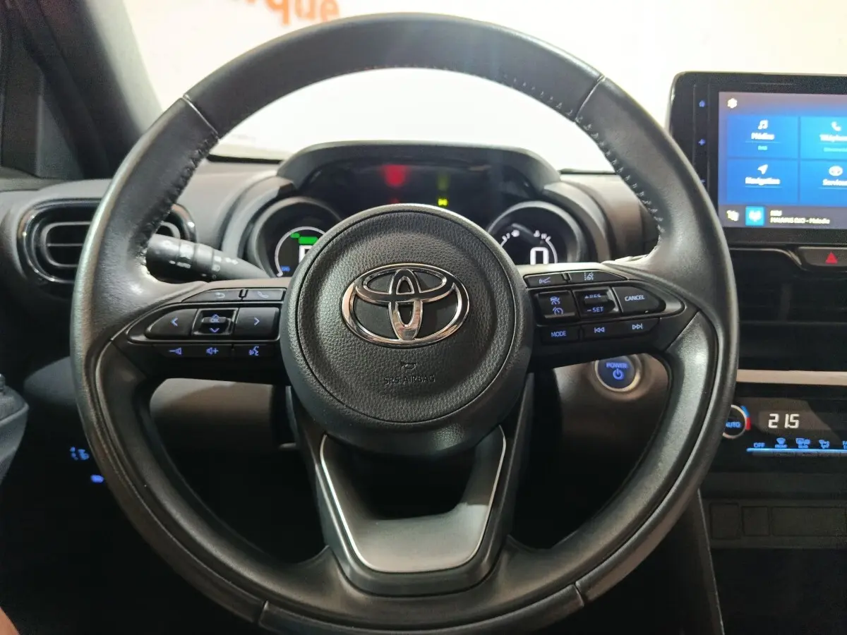 Vue rapprochée du volant cuir noir de la Toyota Yaris Cross 1.5 Hybrid 2022 avec commandes multifonctions et tableau de bord numérique.
