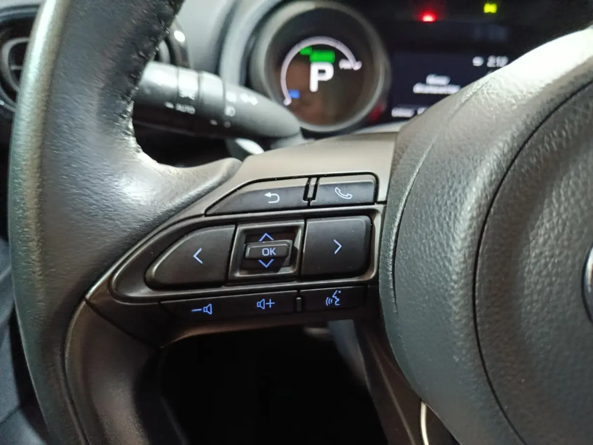 Gros plan sur les commandes au volant à gauche du Toyota Yaris Cross 1.5 Hybrid 116h Design Auto, tableau de bord en arrière-plan.