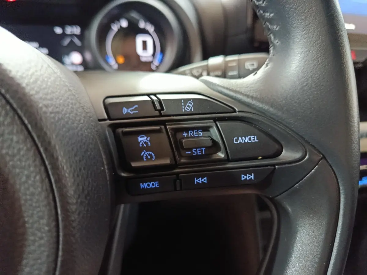 Gros plan sur les commandes du volant cuir noir du Toyota Yaris Cross 1.5 Hybrid 2022, avec régulateur adaptatif et fonctions vocales.