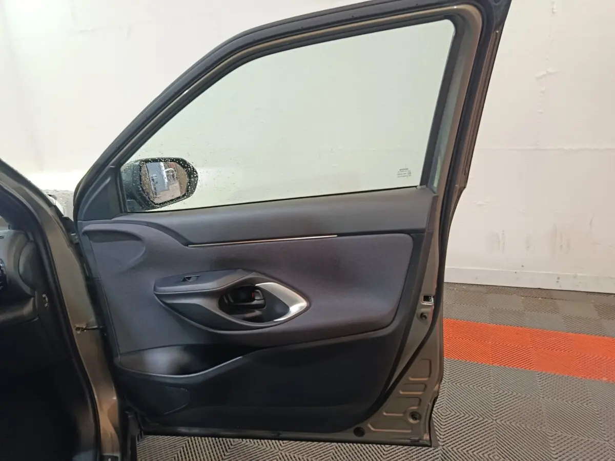 Vue intérieure de la porte avant gauche gris foncé de la Toyota Yaris Cross 1.5 Hybrid 2022 avec poignée noire et garniture tissu.