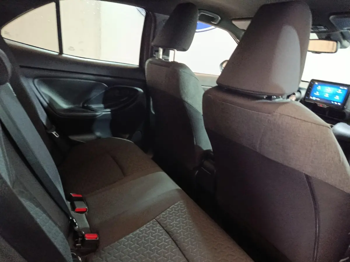 Vue intérieure arrière côté gauche de la Toyota Yaris Cross 2022, sièges tissu gris foncé avec écran tactile avant visible.