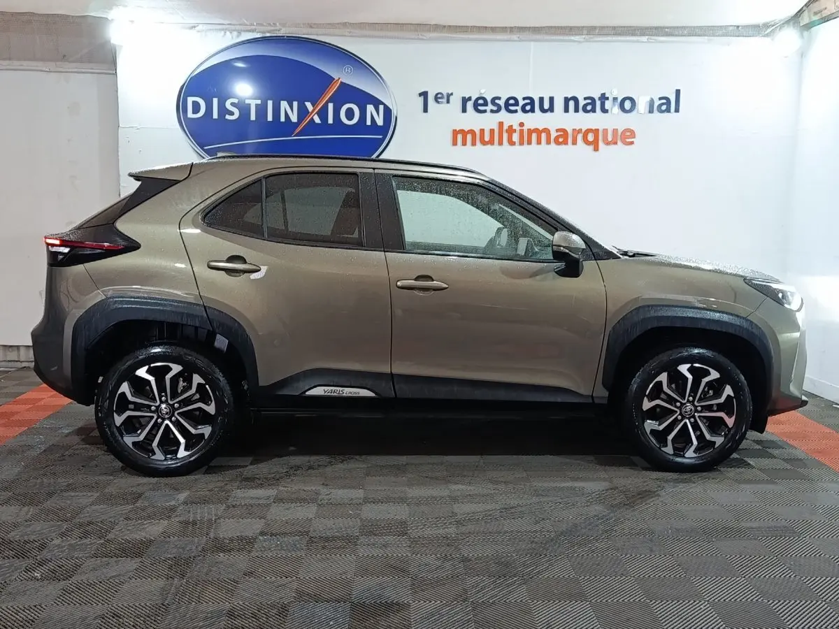 Toyota Yaris Cross gris foncé vue de profil côté gauche, avec jantes alliage et protections noires autour des roues.