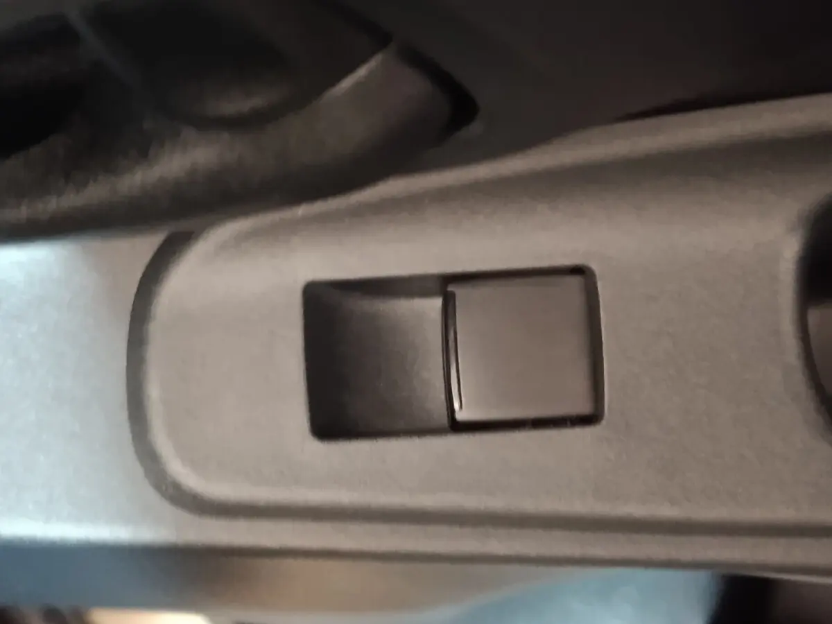 Gros plan sur le bouton de commande de la vitre côté conducteur dans l'habitacle gris foncé d'une Toyota Yaris Cross 2022.