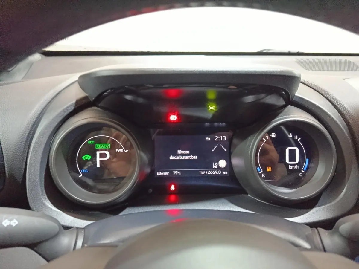 Vue rapprochée du combiné d'instruments digital de la Toyota Yaris Cross 1.5 Hybrid 116h, affichant un avertissement de niveau carburant bas.