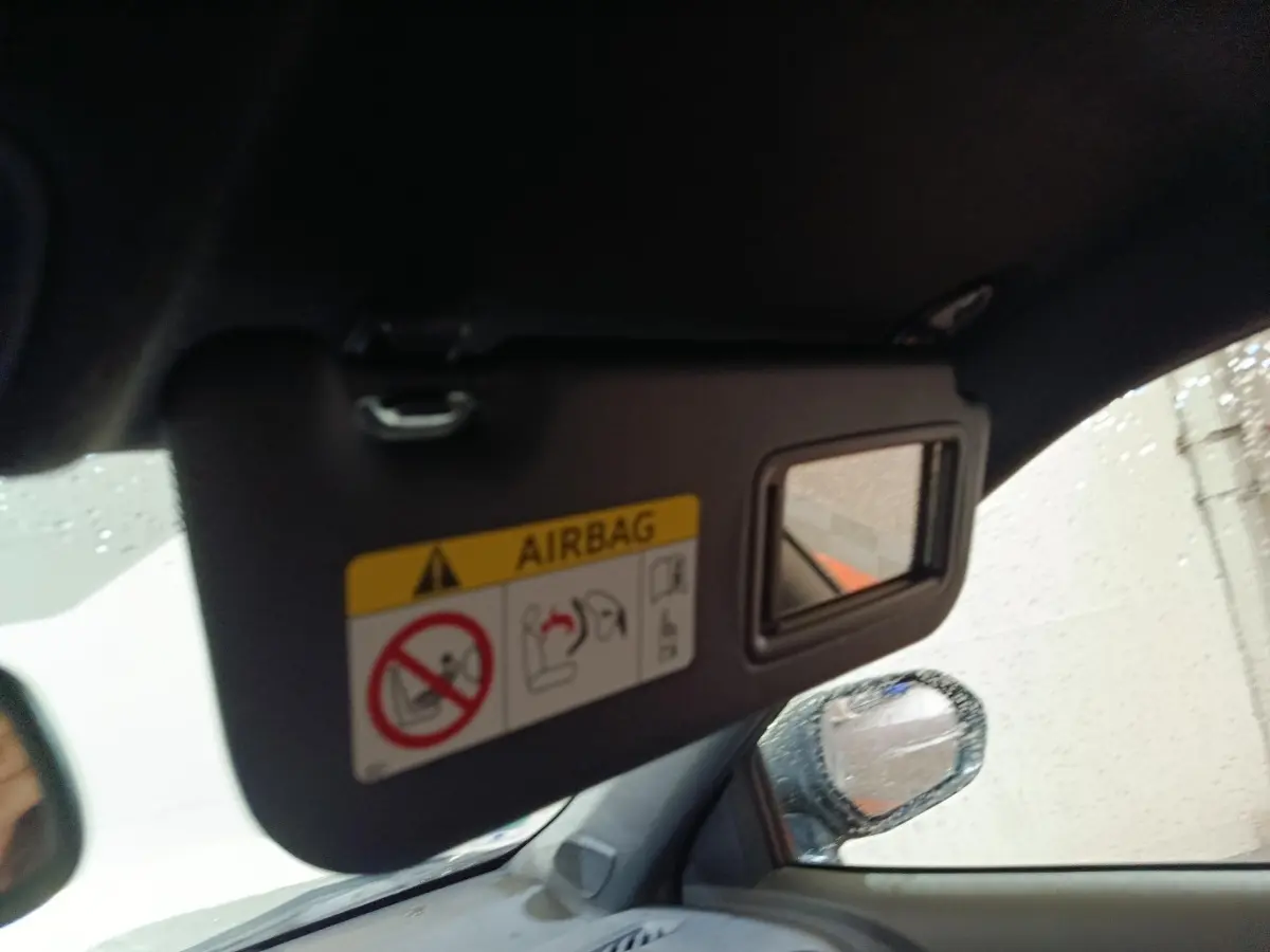 Détail intérieur du pare-soleil côté conducteur avec miroir et avertissement airbag, rétroviseur extérieur visible sous la pluie.