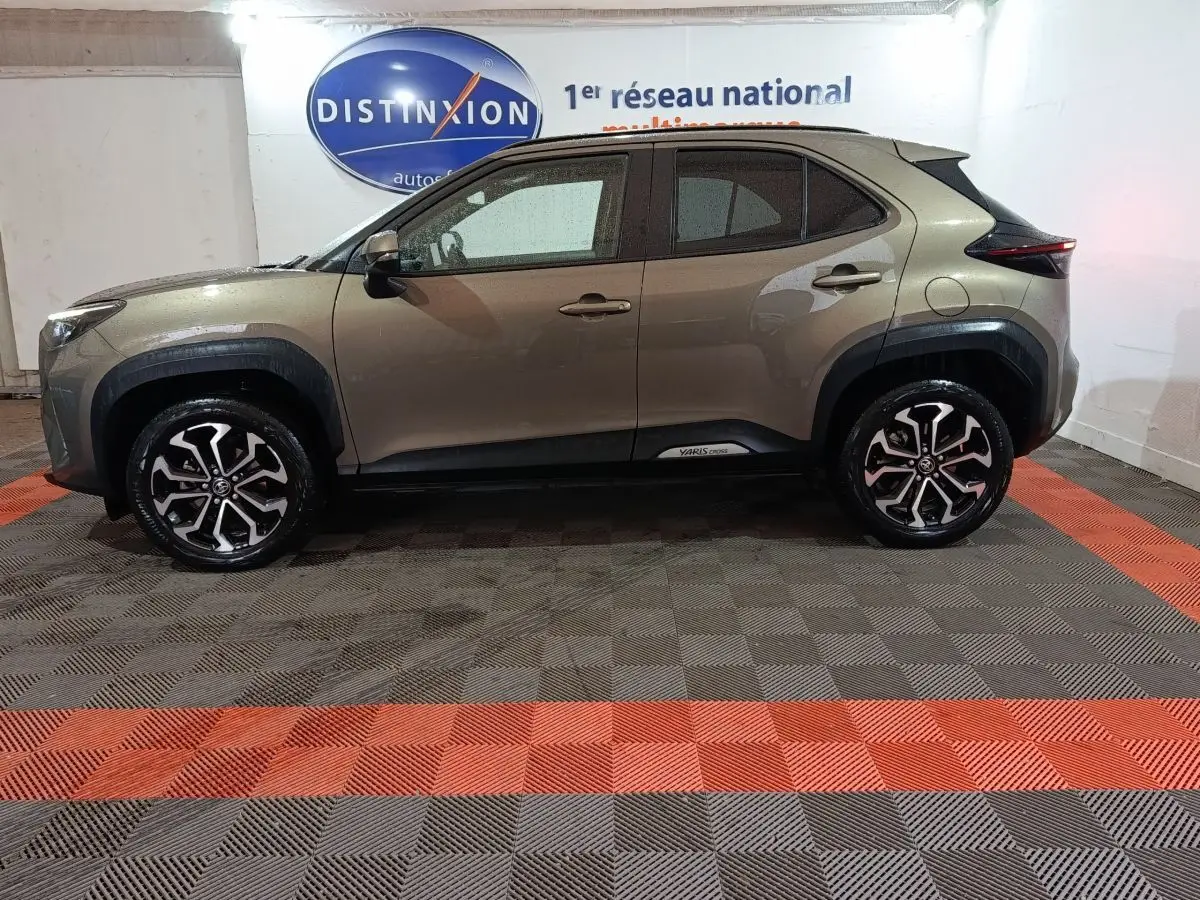 Vue de profil côté gauche d'une Toyota Yaris Cross gris foncé avec jantes alliage et protections noires autour des passages de roues.