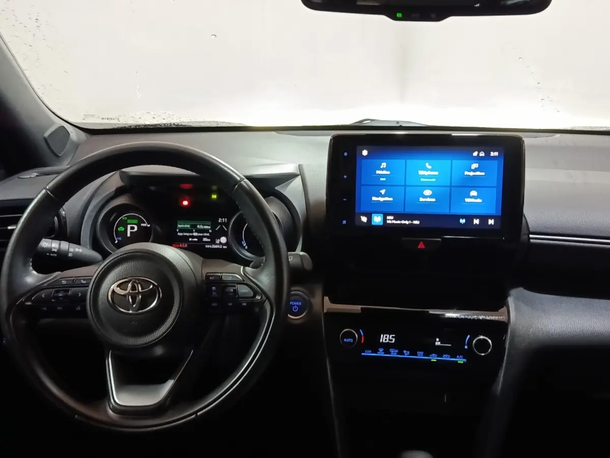 Vue intérieure frontale du tableau de bord et volant cuir noir du Toyota Yaris Cross hybride 2022 avec écran tactile central allumé.