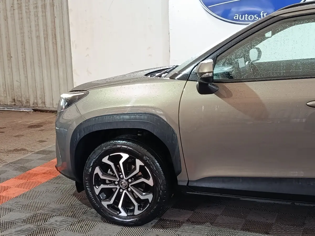 Vue de profil avant droit du Toyota Yaris Cross gris foncé, mettant en valeur la roue alliage et les protections d'ailes noires.