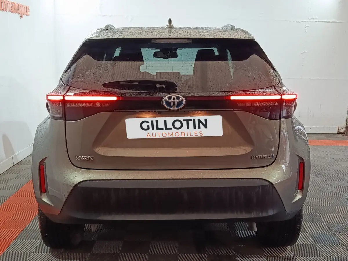 Vue arrière d'une Toyota Yaris Cross gris foncé avec feux arrière LED allumés dans un garage.