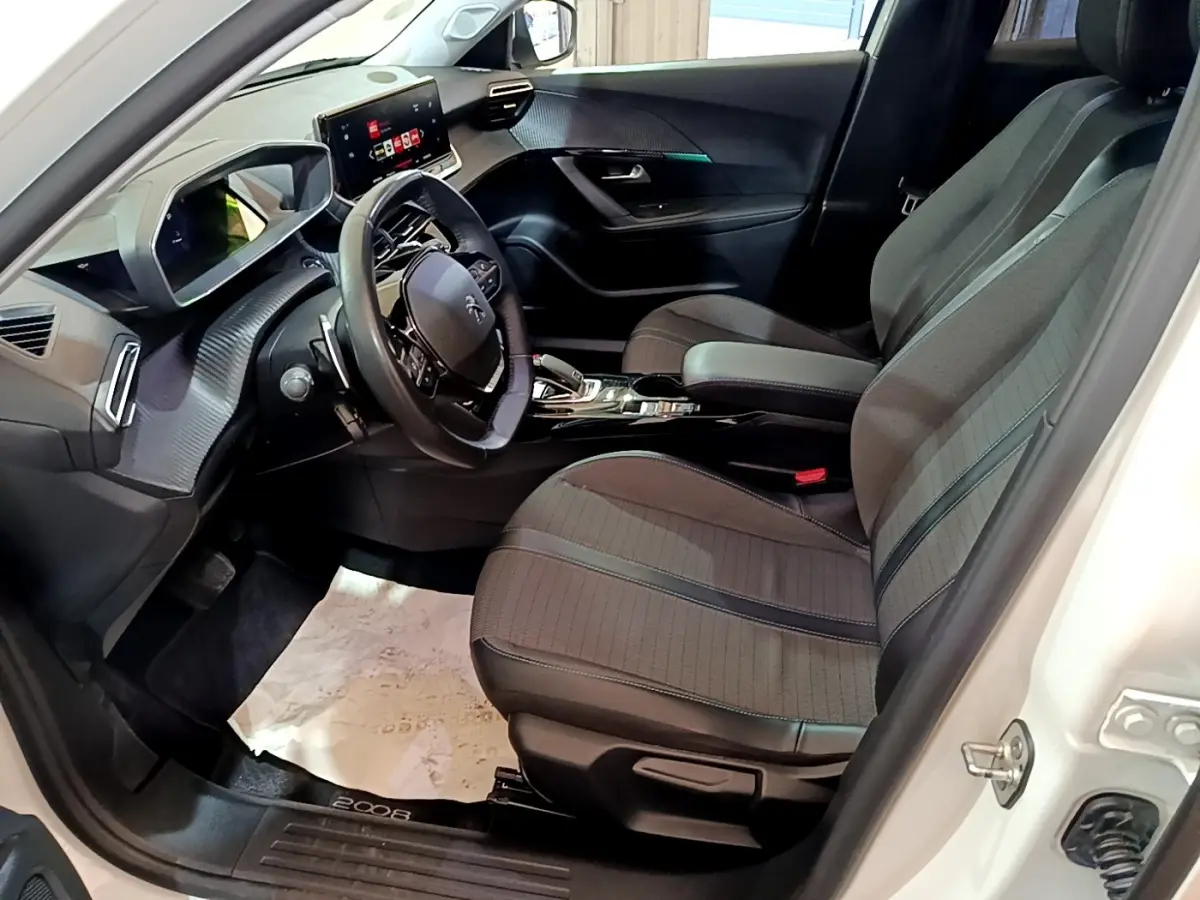 Vue intérieure côté conducteur du Peugeot 2008 blanc, mettant en valeur le volant cuir multifonctions et la console centrale moderne.