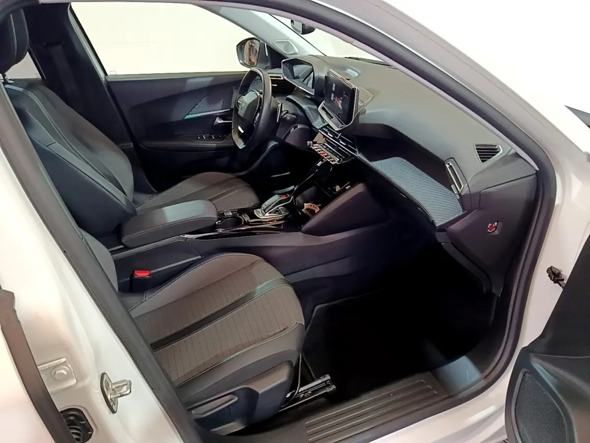 Intérieur côté conducteur du Peugeot 2008 blanc, montrant sièges tissu, volant cuir multifonctions et tableau de bord moderne.