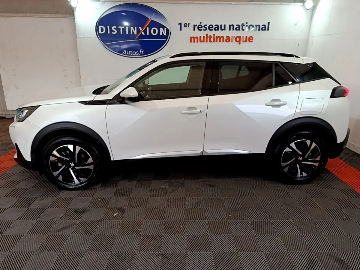 Vue de profil côté gauche d'un Peugeot 2008 blanc 2021 avec jantes alliage noires et toit noir contrasté.