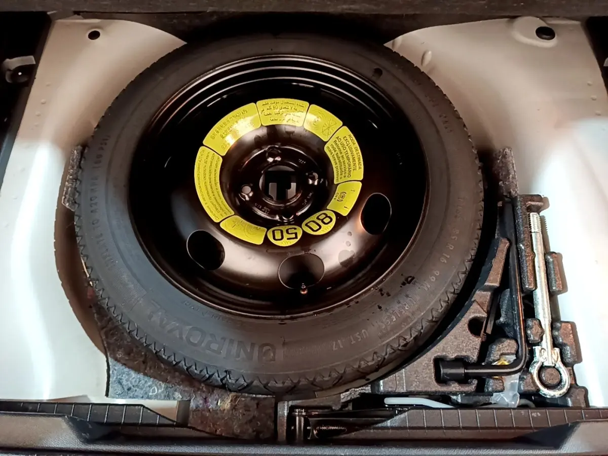 Vue plongeante sur la roue de secours noire avec étiquette jaune et outils de bord dans le coffre d’un Peugeot 2008 blanc.