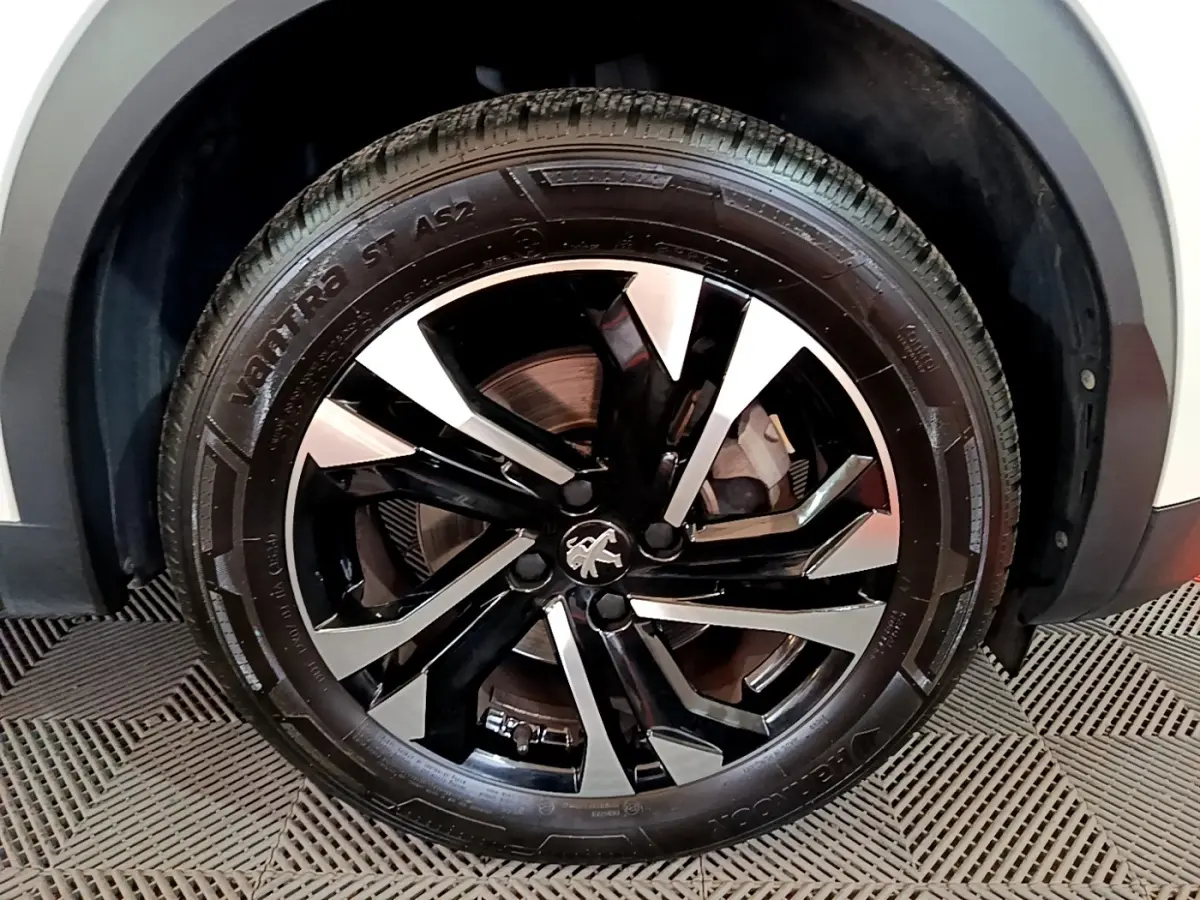 Gros plan sur la roue avant droite du Peugeot 2008 blanc, mettant en valeur la jante alliage noire et argentée au design moderne.