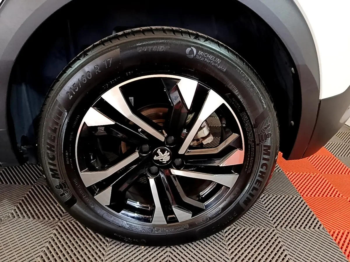 Gros plan sur la roue avant droite d’un Peugeot 2008 blanc, jante alliage noire et argent avec logo lion central.