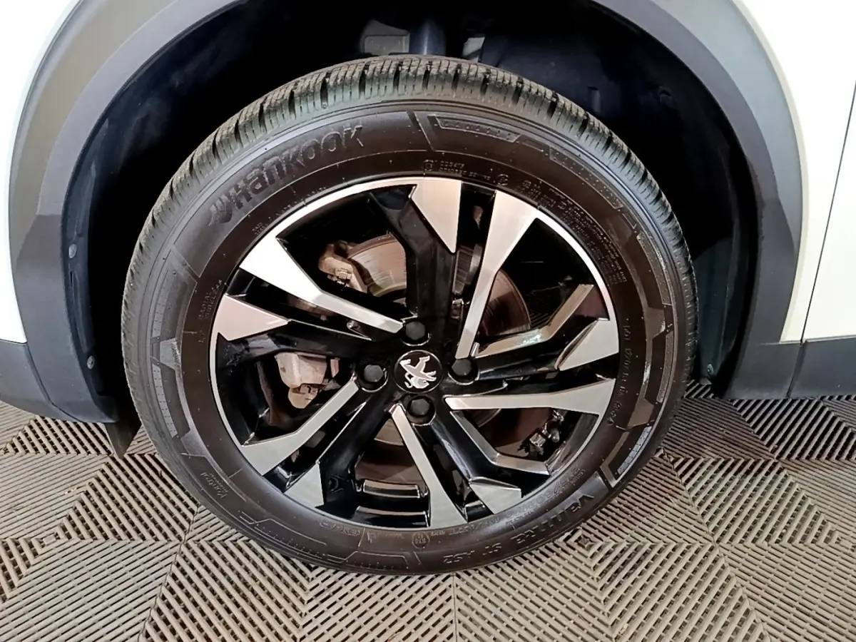 Gros plan sur la roue avant droite d’un Peugeot 2008 blanc, jante alliage noire et argentée au design moderne.
