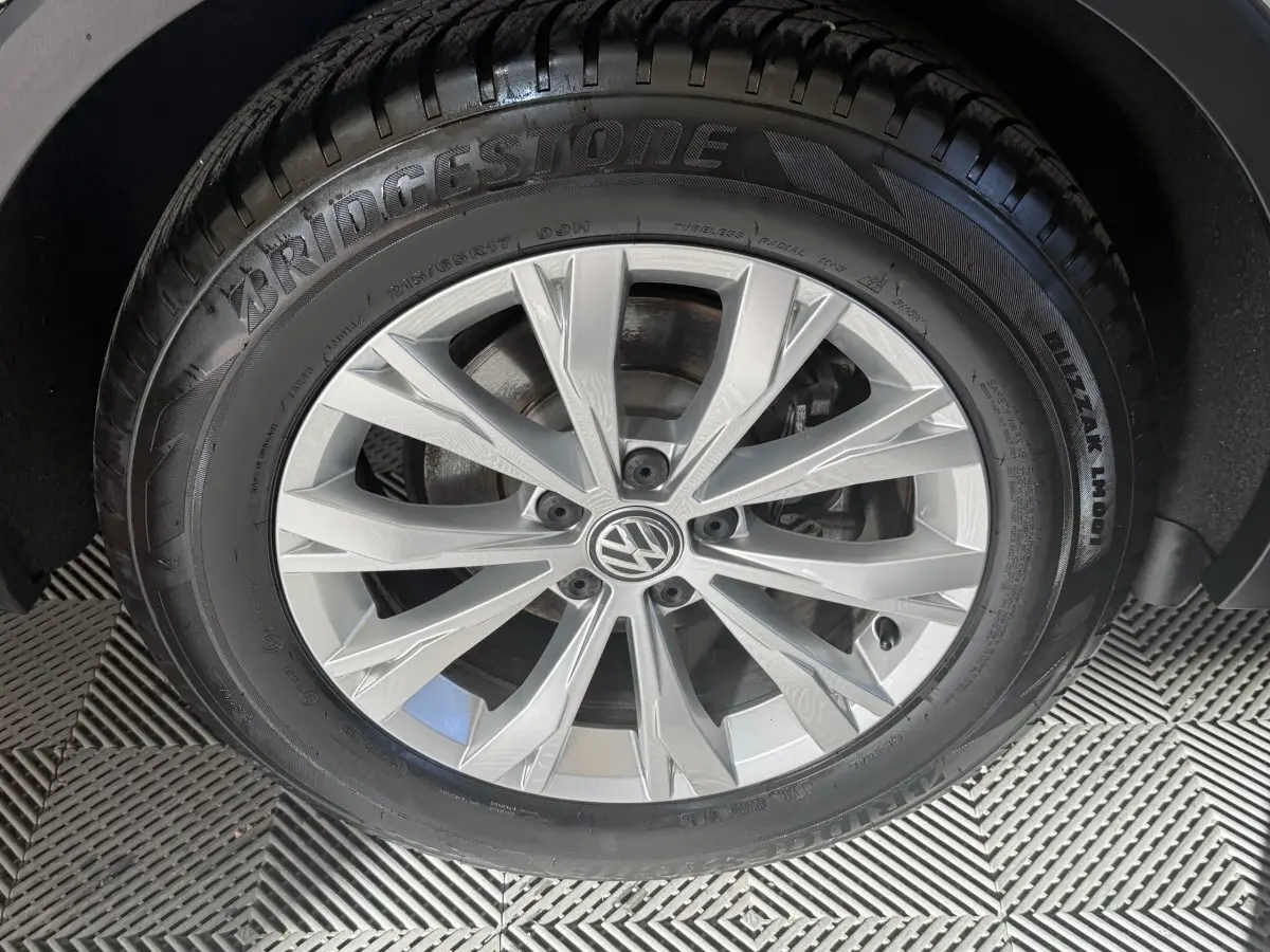 Gros plan sur la roue avant droite du Volkswagen Tiguan gris clair, mettant en valeur la jante alliage et le pneu Bridgestone.