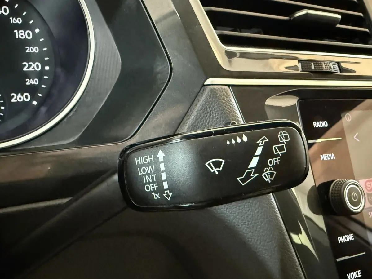 Gros plan sur la commande des essuie-glaces du Volkswagen Tiguan gris clair, avec tableau de bord et écran tactile en arrière-plan.