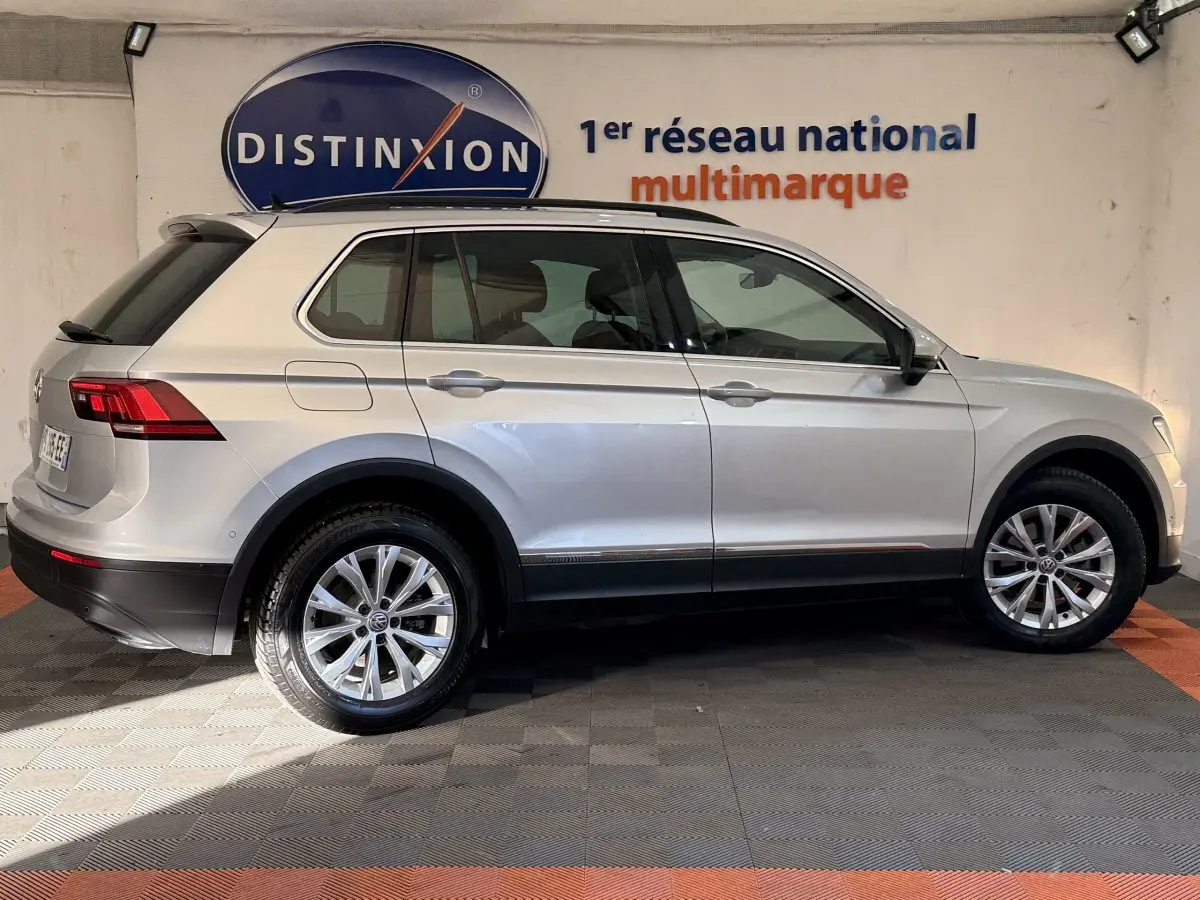 Profil droit d'un Volkswagen Tiguan gris clair 2020 garé en intérieur avec jantes alliage et barres de toit noires.