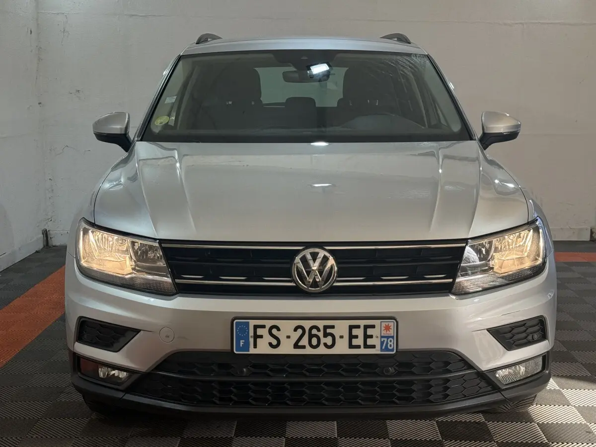 Vue frontale d'un Volkswagen Tiguan gris clair 2020 avec phares allumés et calandre noire distinctive.