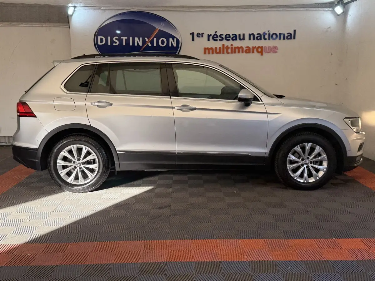 Vue de profil côté gauche d'un Volkswagen Tiguan gris clair garé en intérieur sur sol à damiers, avec logo Distinxion en arrière-plan.