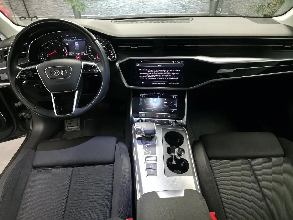 Vue intérieure avant de l'Audi A6 2022 S line, tableau de bord noir avec écran tactile et volant multifonction cuir.