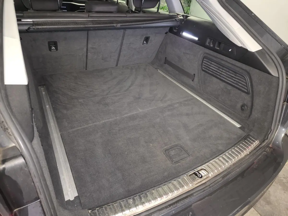 Coffre ouvert vu de l'arrière d'une Audi A6 Avant gris, avec tapis de sol noir et finitions métalliques visibles.