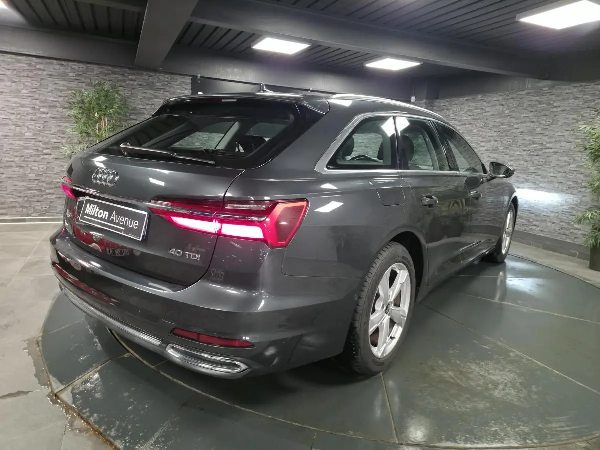 Audi A6 Avant gris en 3/4 arrière droit, feux LED allumés et jantes 5 branches dans un showroom intérieur.