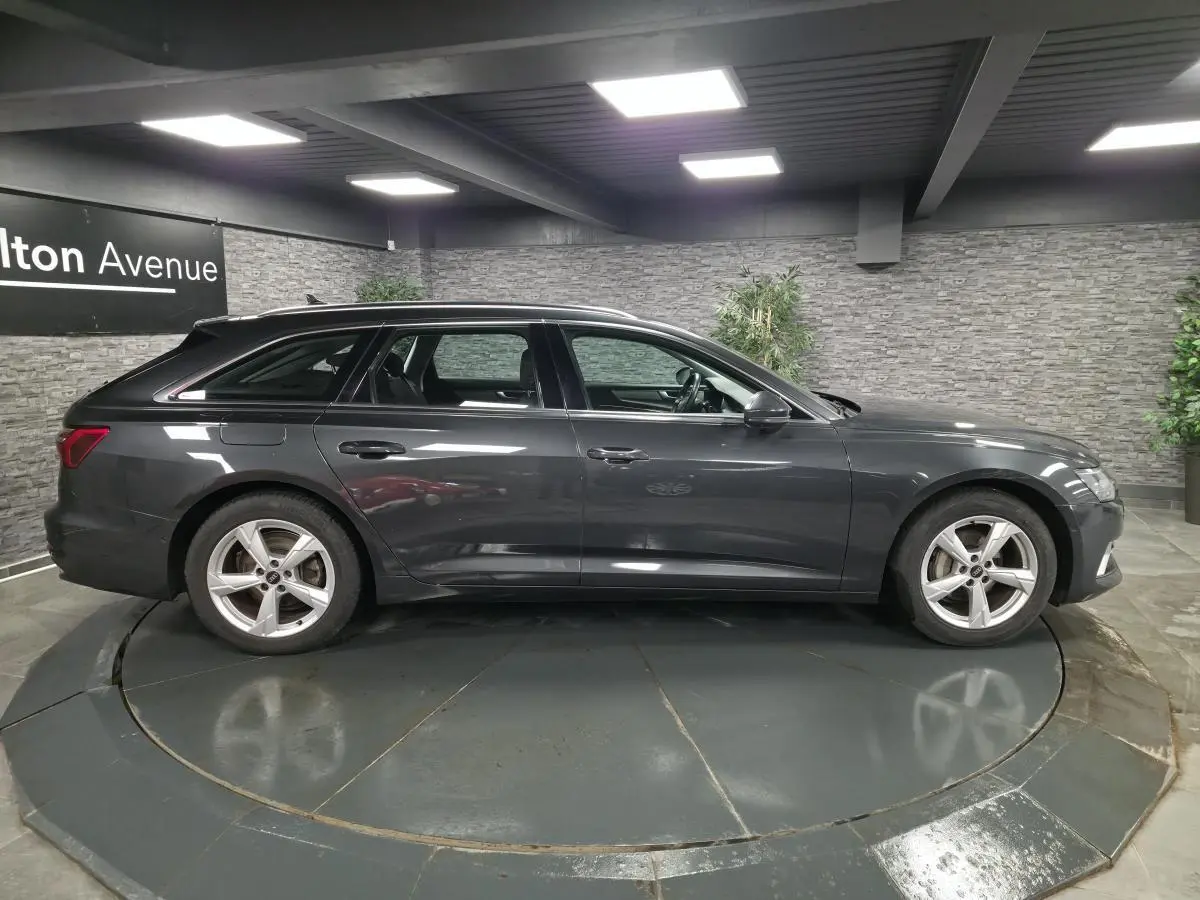 Audi A6 Avant gris en profil droit dans un showroom avec jantes 5 branches et toit ouvrant visible.