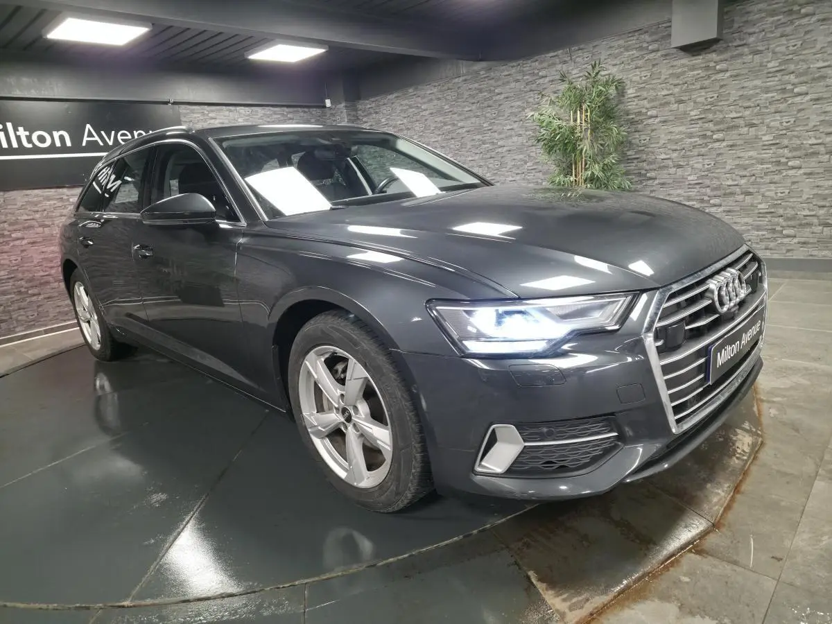 Audi A6 Avant gris métallisé vue 3/4 avant droit avec phares LED allumés en intérieur showroom.