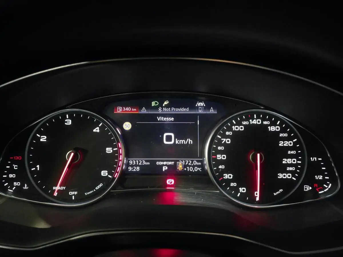 Vue rapprochée du tableau de bord numérique de l'Audi A6 gris, affichant la vitesse à 0 km/h et divers indicateurs.