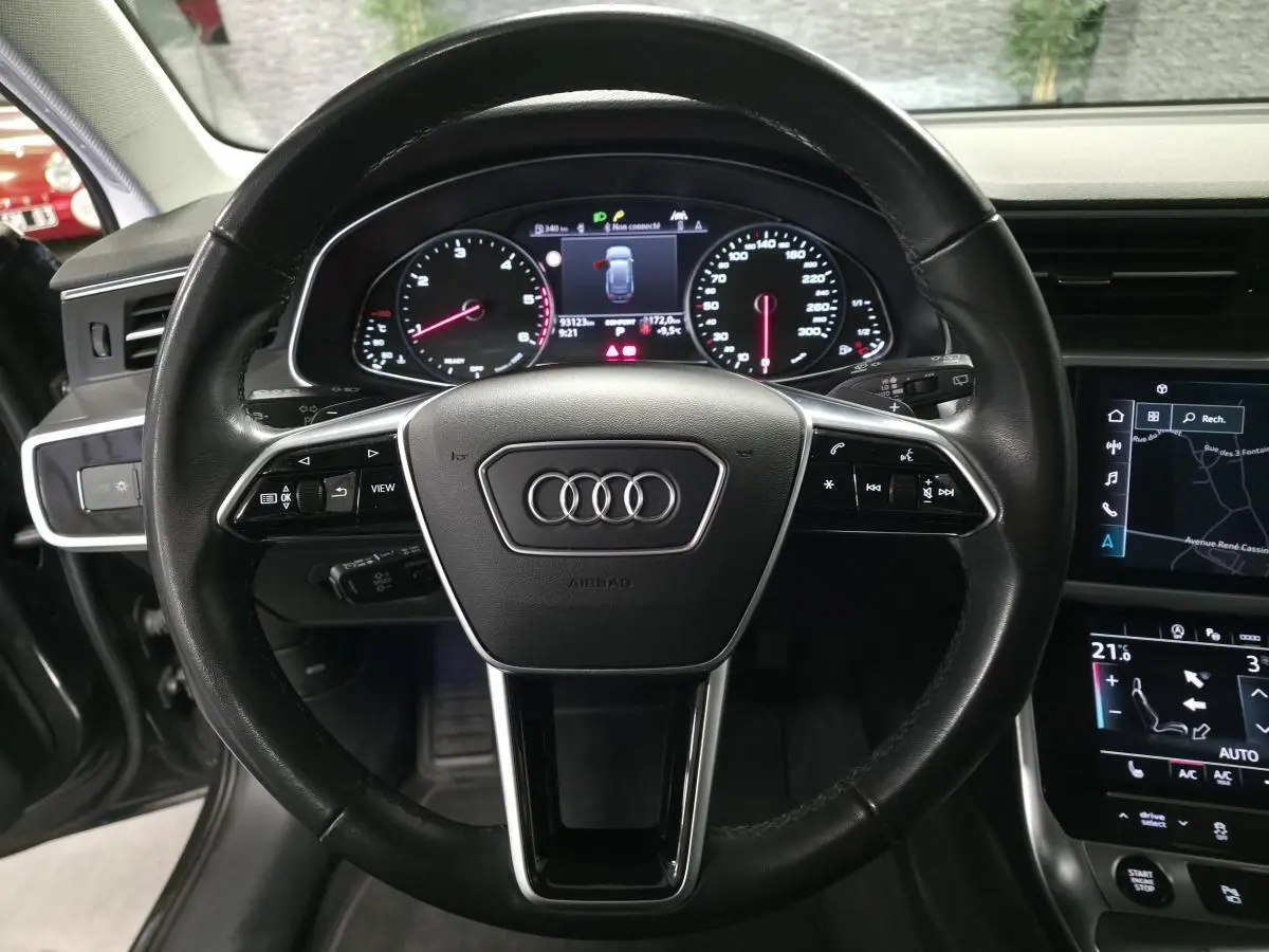 Vue intérieure centrée sur le volant noir en cuir d'une Audi A6 2022 avec tableau de bord digital et écran tactile.