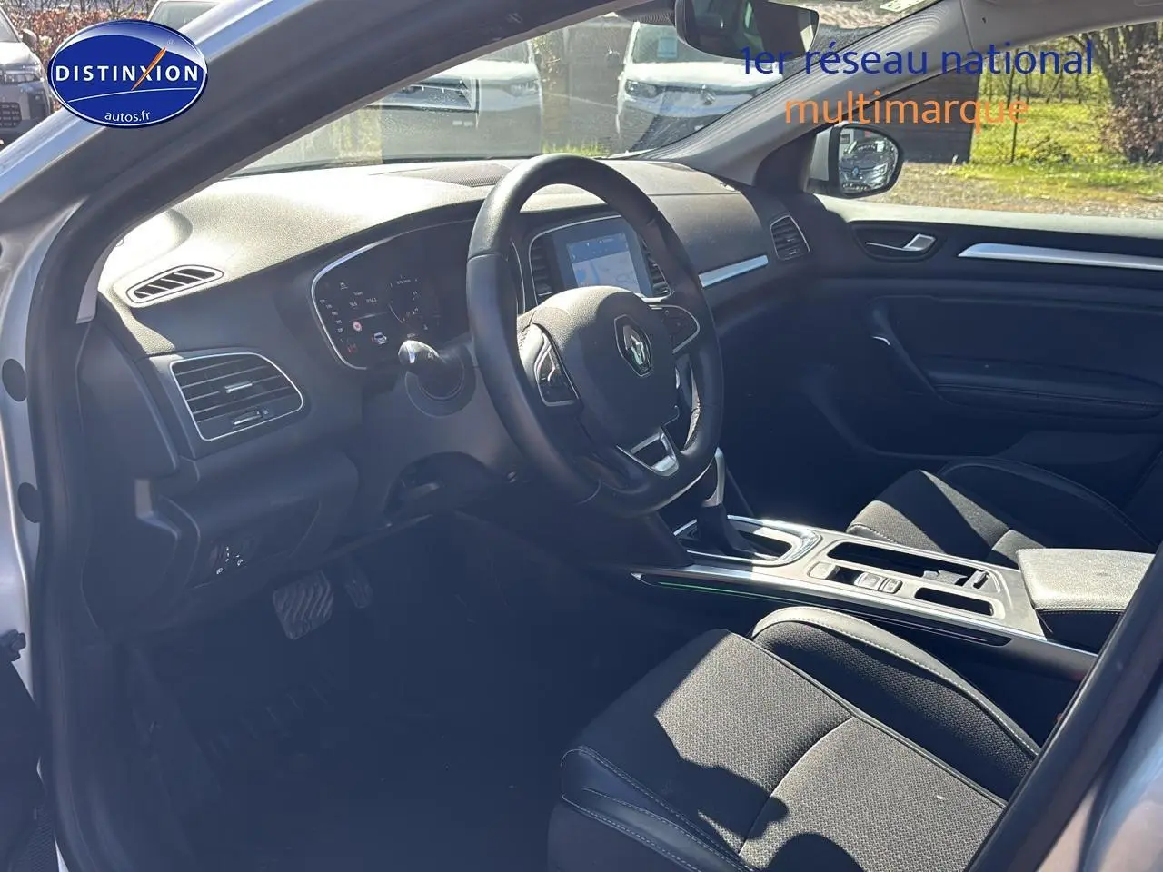 Intérieur côté conducteur de Renault Mégane IV 2023, volant multifonction et sièges tissu noirs visibles.