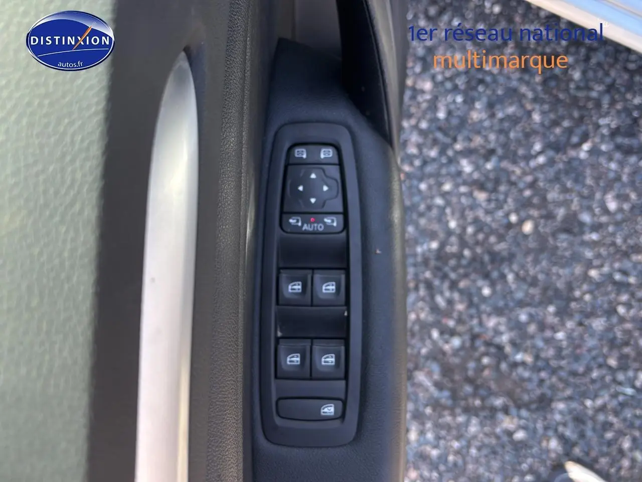 Gros plan sur la commande des vitres électriques côté conducteur d'une Renault Mégane IV gris Highland, avec fond bitume.