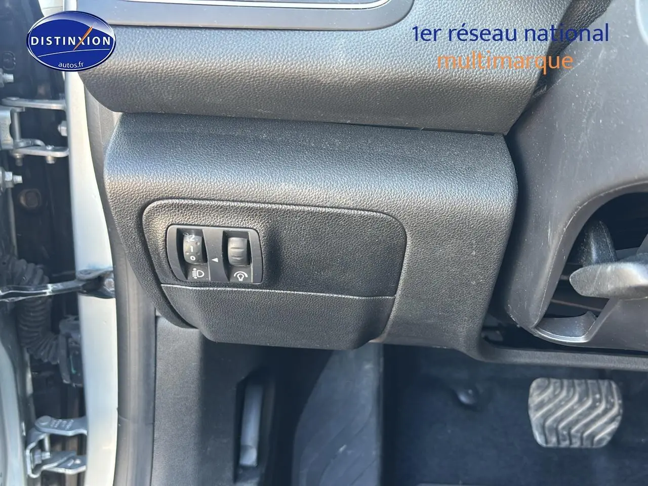 Détail intérieur côté gauche avec commandes de réglage des phares et pédale d’embrayage visible sur Renault Mégane IV gris Highland.