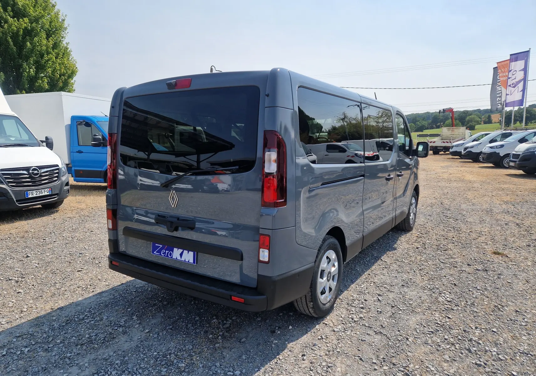 Vue 3/4 arrière droite d’un Renault Trafic Combi gris urbain, avec vitres teintées et hayon fermé sur parking.