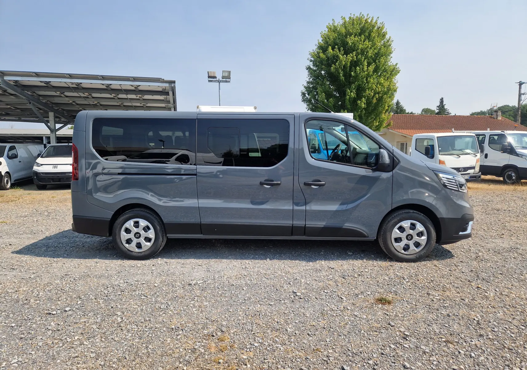 Vue latérale droite du Renault Trafic Combi gris urbain 2026 avec fenêtres teintées et jantes acier.