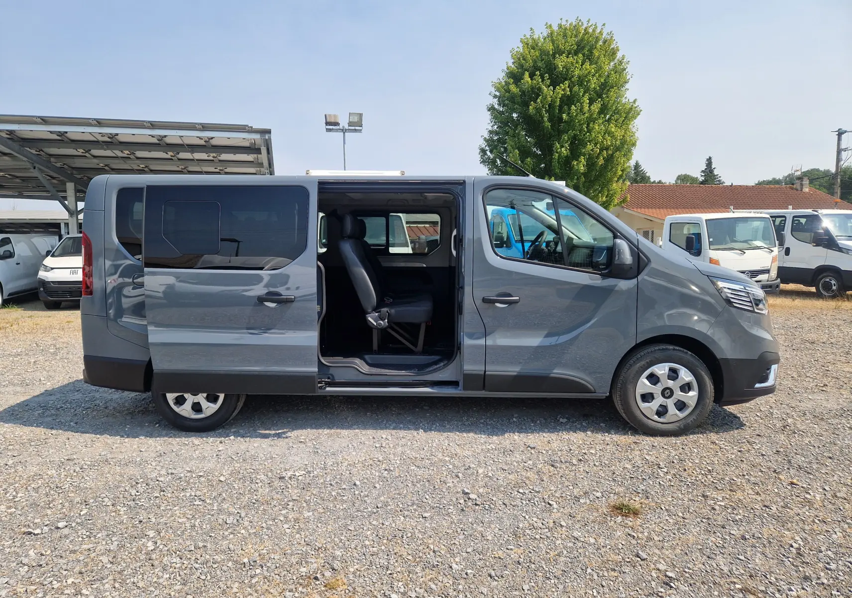 Renault Trafic Combi gris urbain vu de profil droit avec porte coulissante ouverte montrant l'intérieur 8 places.