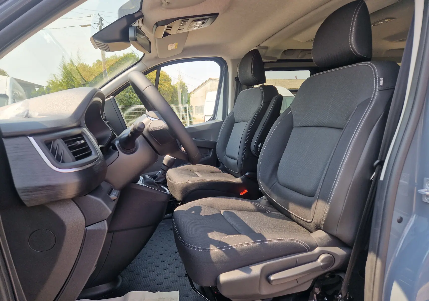 Vue intérieure côté conducteur du Renault Trafic Combi gris urbain 2026, montrant les sièges avant et le tableau de bord.