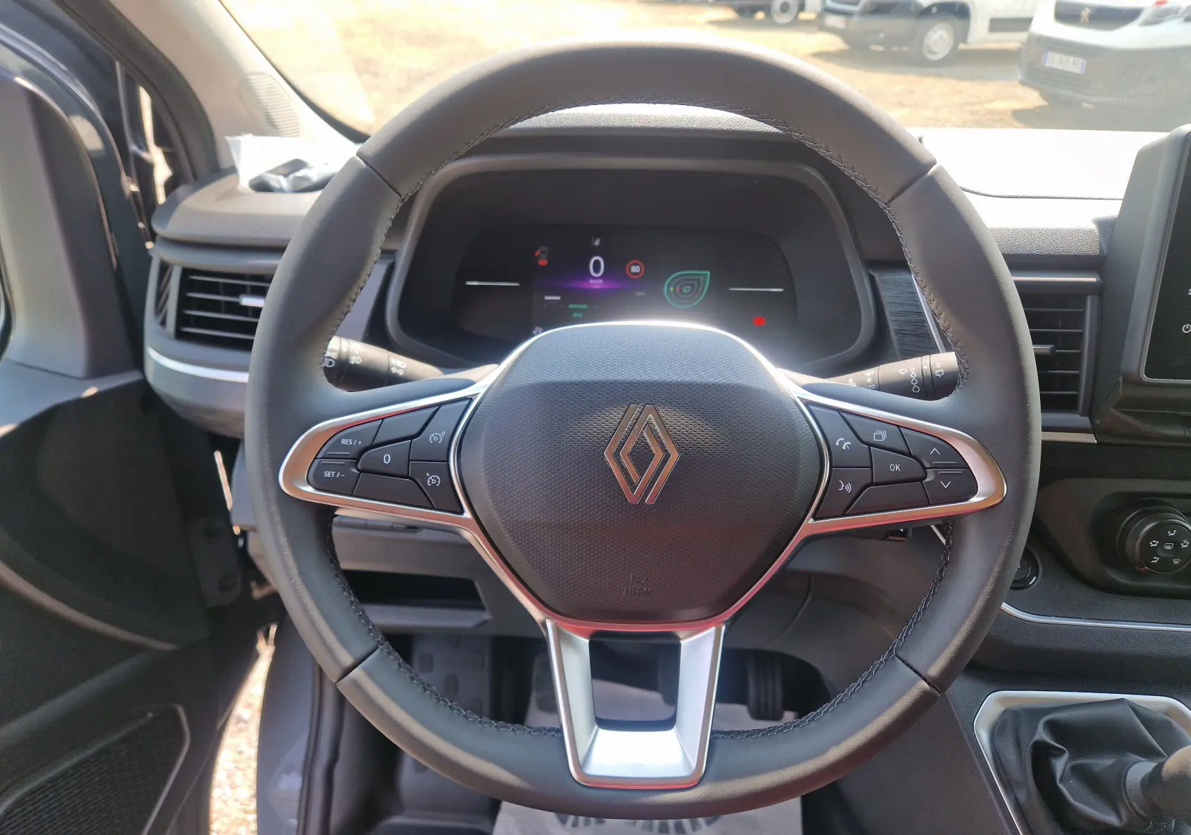 Vue intérieure centrée sur le volant du Renault Trafic Combi gris urbain, avec commandes intégrées et tableau de bord numérique.