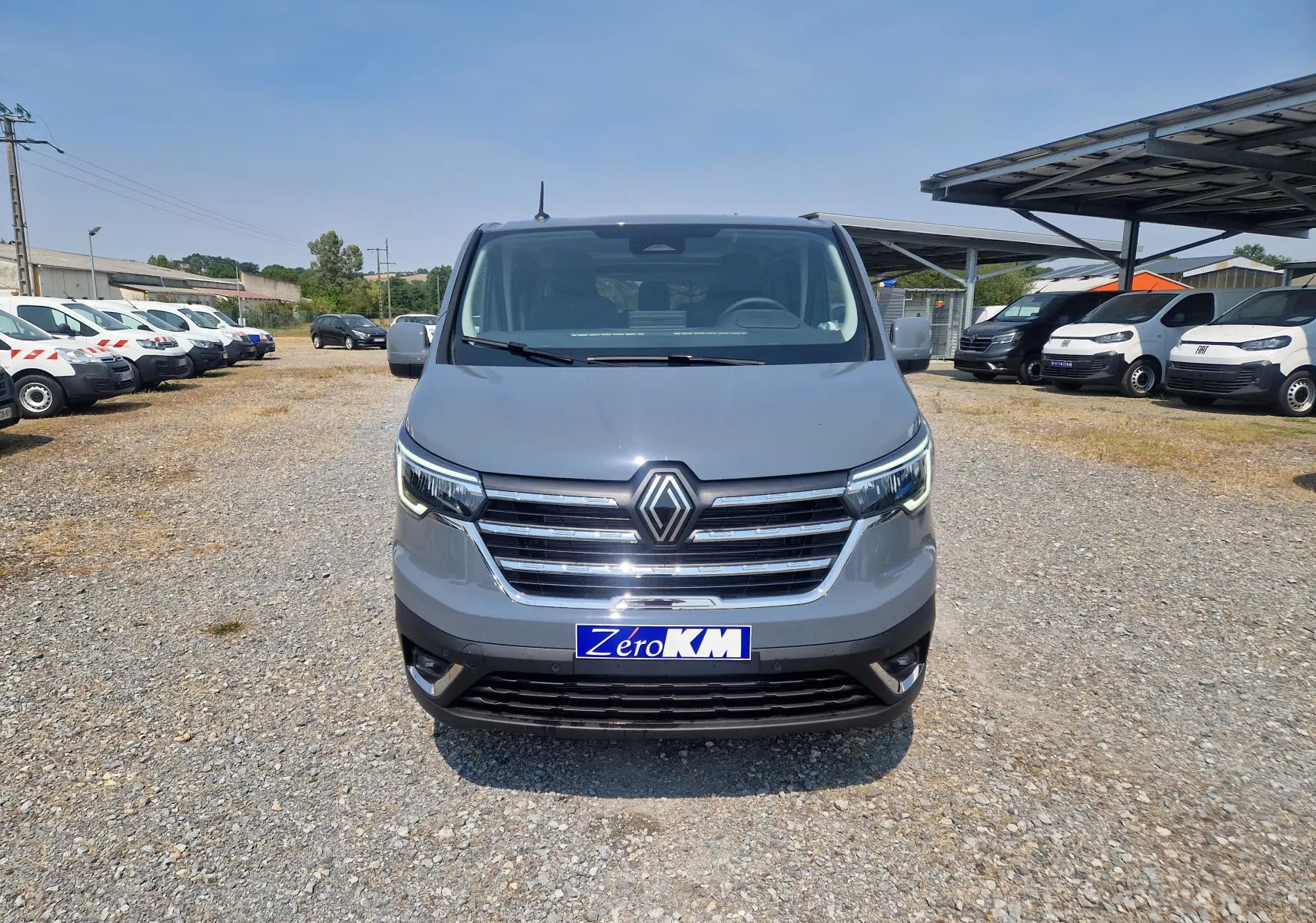 Vue frontale d’un Renault Trafic Combi gris urbain 2026, avec calandre chromée et plaque Zero KM visible.