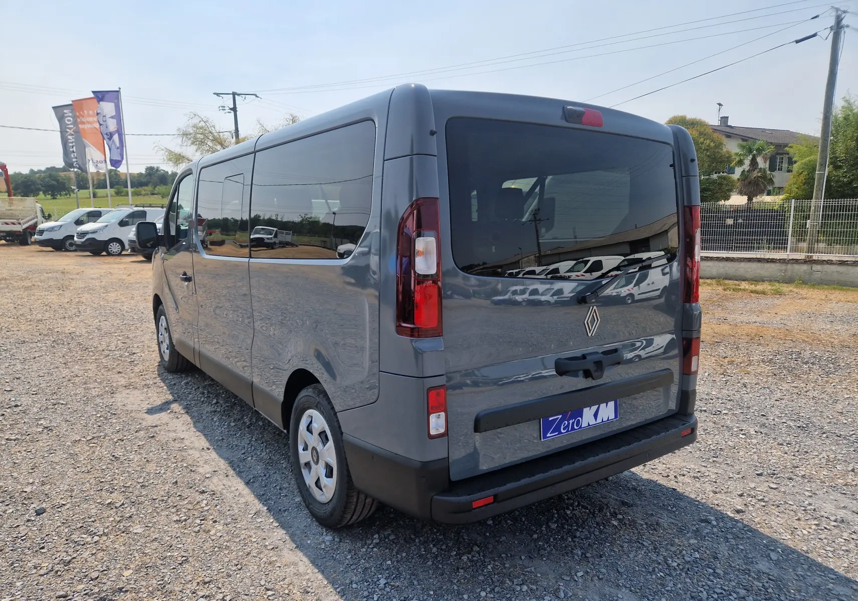 Vue 3/4 arrière droite du Renault Trafic Combi gris urbain 2026 avec vitres teintées et hayon fermé sur parking.
