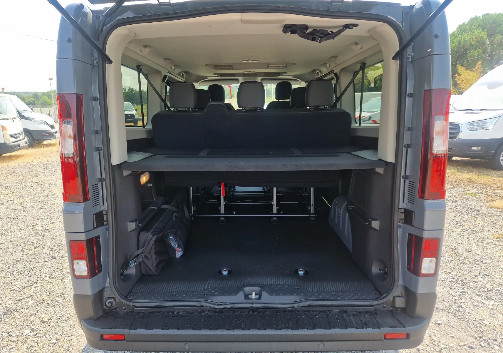 Vue arrière ouverte du Renault Trafic Combi gris urbain 2026, montrant l'espace de chargement avec sièges arrière et fixation fauteuil roulant.