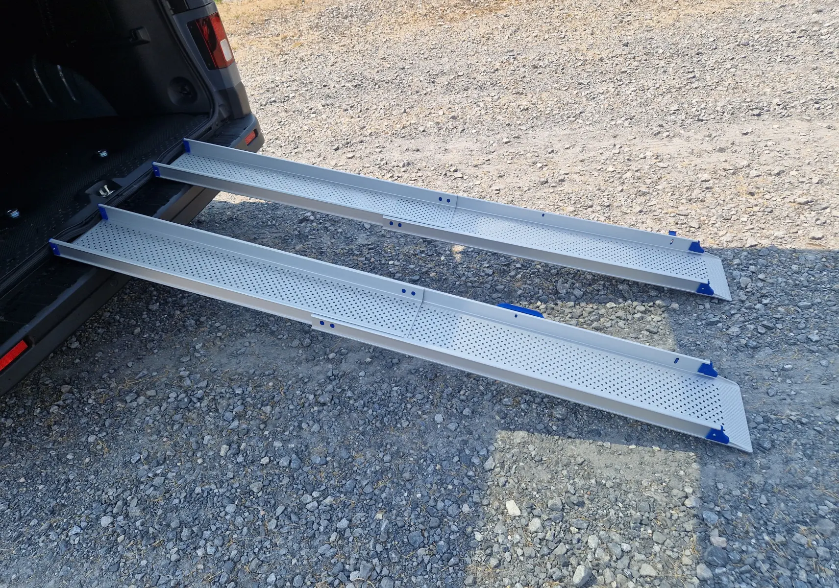 Vue arrière en 3/4 du Renault Trafic Combi gris urbain avec ses rampes d'accès amovibles en aluminium déployées au sol.